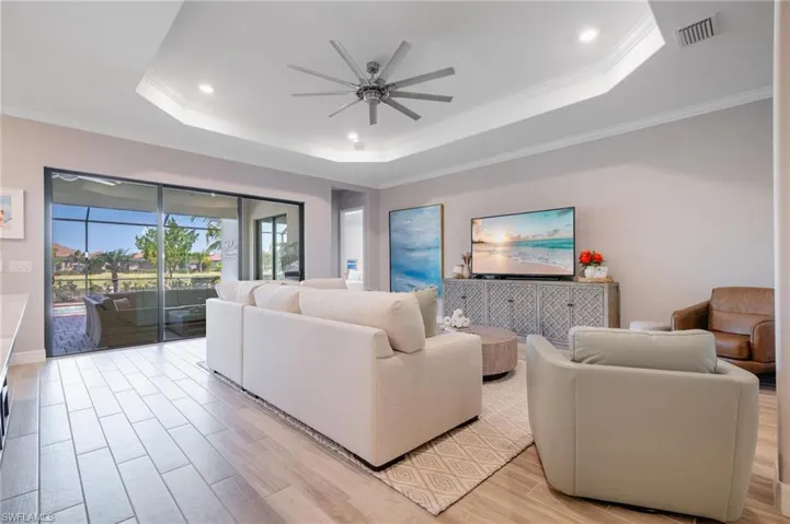 Living room featuring ceiling fan, a raised ceiling, crown molding, and light hardwood / wood-style floors