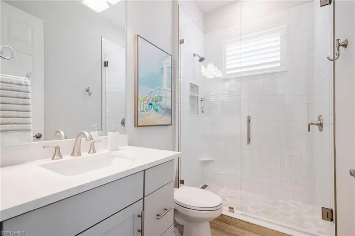 Bathroom featuring wood-type flooring, vanity, toilet, and a shower with door