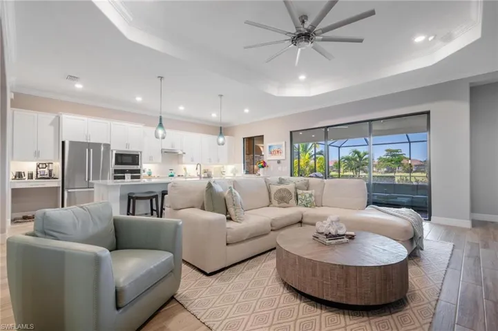 Living room featuring ornamental molding, ceiling fan, a raised ceiling, and light hardwood / wood-style flooring