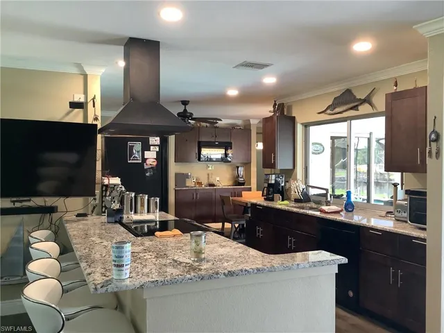 Kitchen with light stone counters, island exhaust hood, a breakfast bar, a peninsula, and ornamental molding