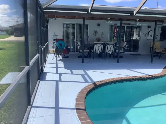 Back of house featuring glass enclosure, a patio area, an outdoor pool, and ceiling fan