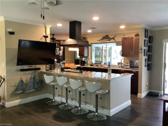 Kitchen with ornamental molding, island range hood, a peninsula, light stone countertops, and dark wood-style floors
