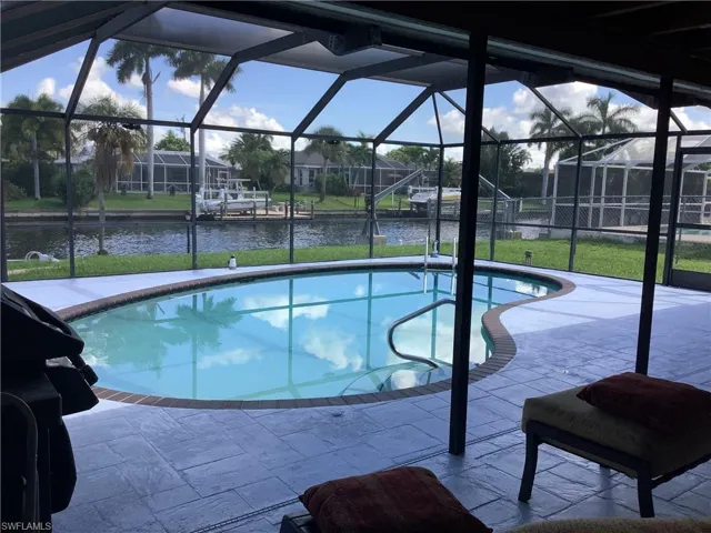 Swimming pool with a sunroom, a water view, a yard, a patio area, and a lanai