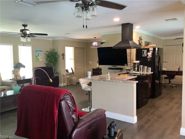 Kitchen featuring a ceiling fan, range hood, open floor plan, crown molding, and light stone countertops