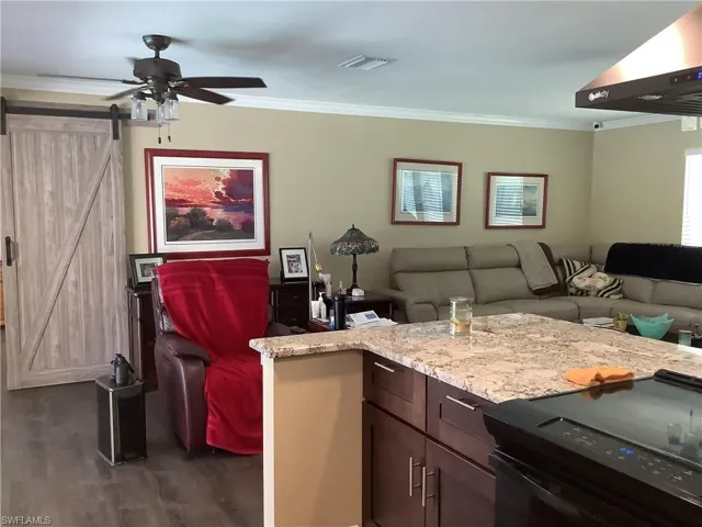 Living area with a barn door, crown molding, a ceiling fan, and dark wood finished floors