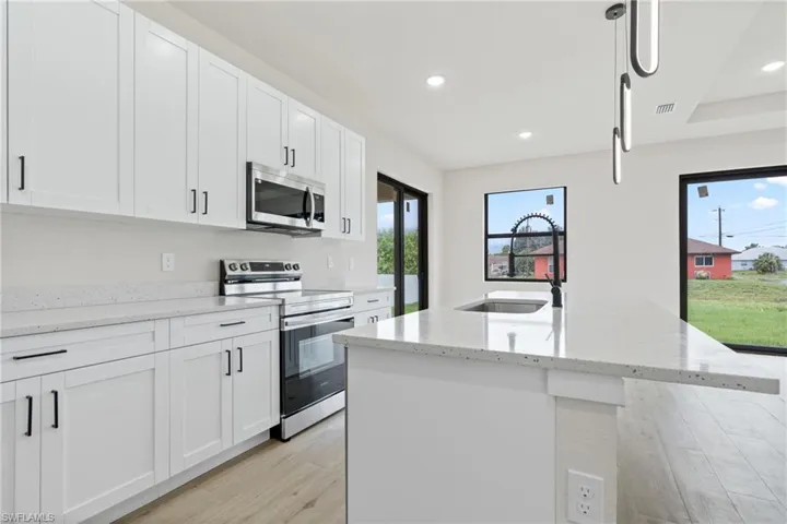 Kitchen featuring range with electric cooktop, a center island with sink, light stone counters, sink, and white cabinets