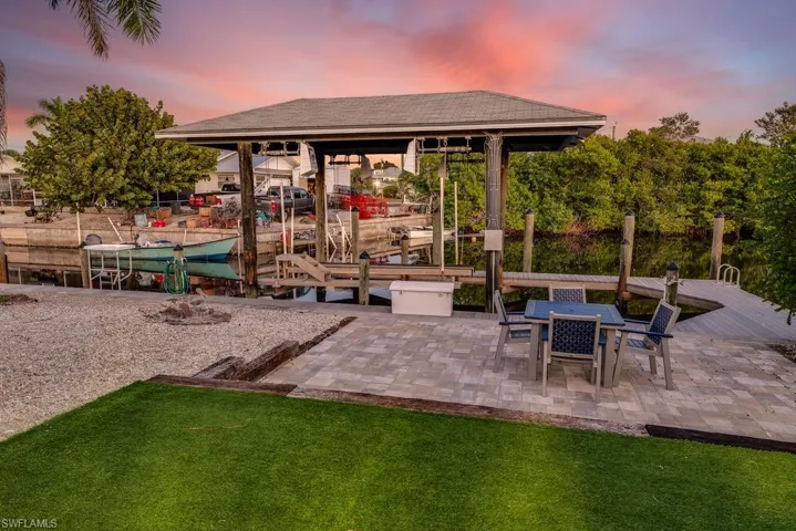 Patio terrace at dusk featuring boat lift, a dock, a patio area, and a yard