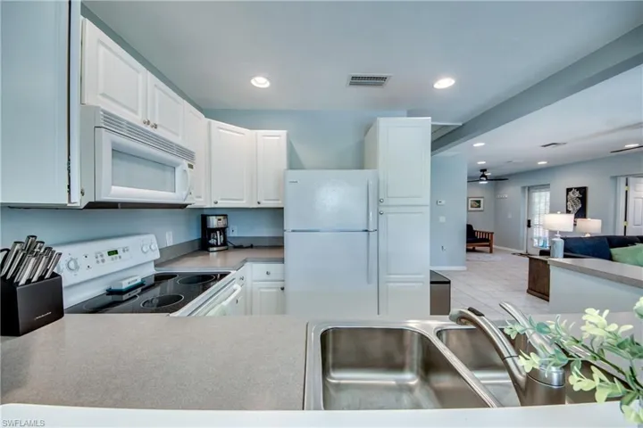Kitchen featuring white appliances, open floor plan, ceiling fan, white cabinets, and light countertops