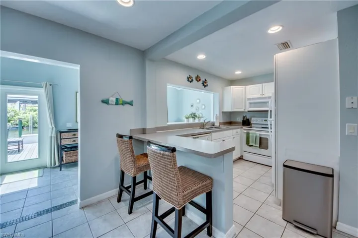 Kitchen with light tile patterned floors, a breakfast bar area, white appliances, white cabinetry, and recessed lighting