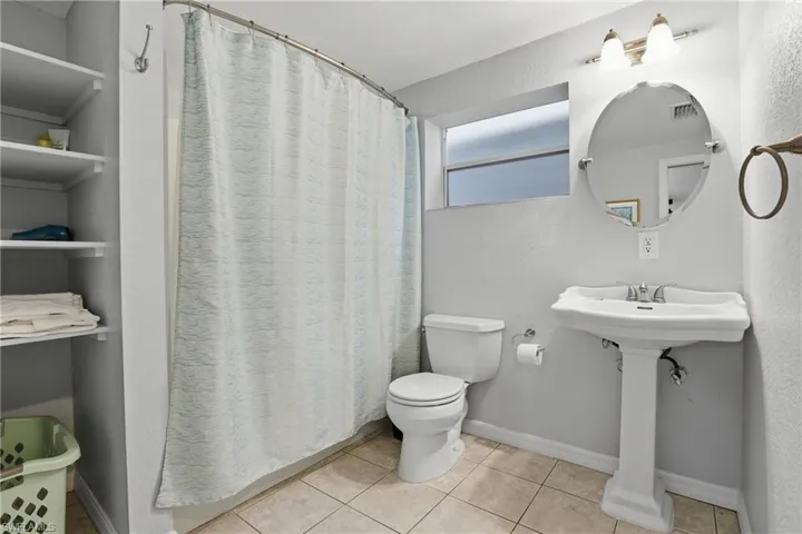 Full bathroom featuring curtained shower, a textured wall, and light tile patterned floors