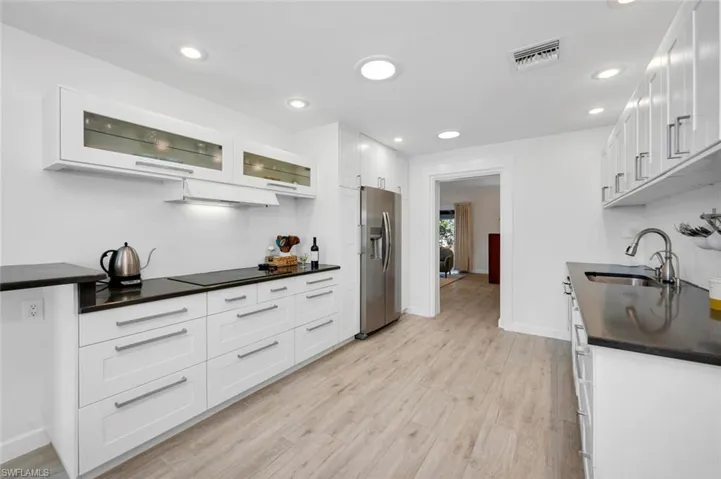 Kitchen featuring stainless steel refrigerator with ice dispenser, induction cooktop, sink, white cabinets, and light wood-style tile floors