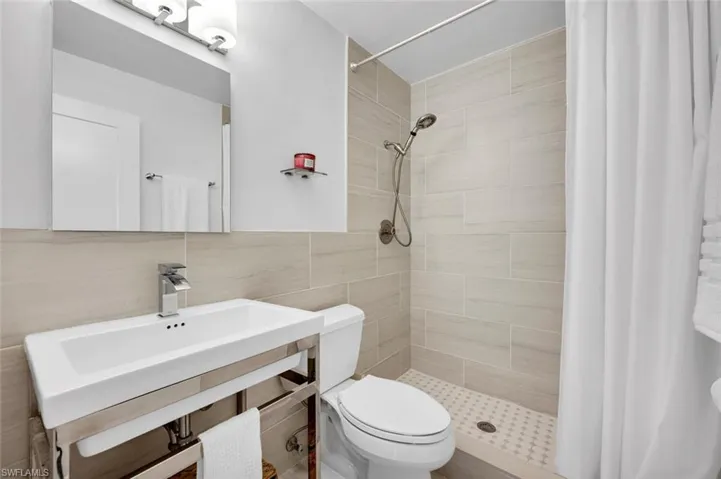 Bathroom with curtained shower, sink, toilet, decorative backsplash, and tile walls