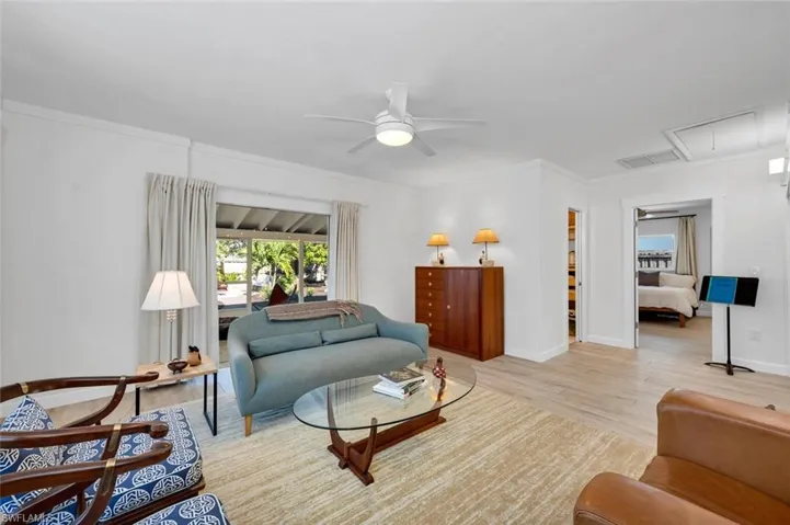 Living room with ceiling fan, light wood-style tile flooring, and crown molding