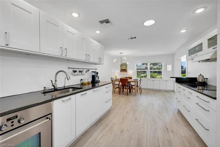 Kitchen featuring white cabinetry, sink, a notable chandelier, induction cooktop, skylight tubes, and light wood-style tile flooring