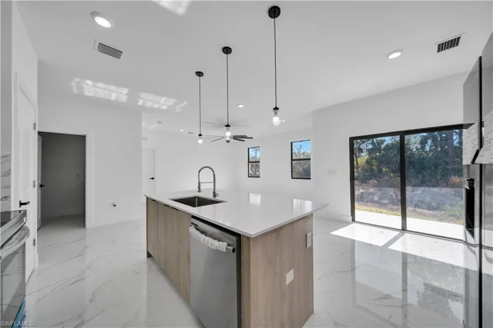 Kitchen featuring modern cabinets, hanging light fixtures, stainless steel appliances, light marble finish floors, and light stone counters