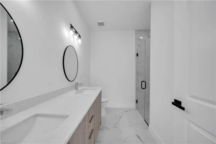 Bathroom featuring a marble finish shower, light marble finish flooring, and double vanity