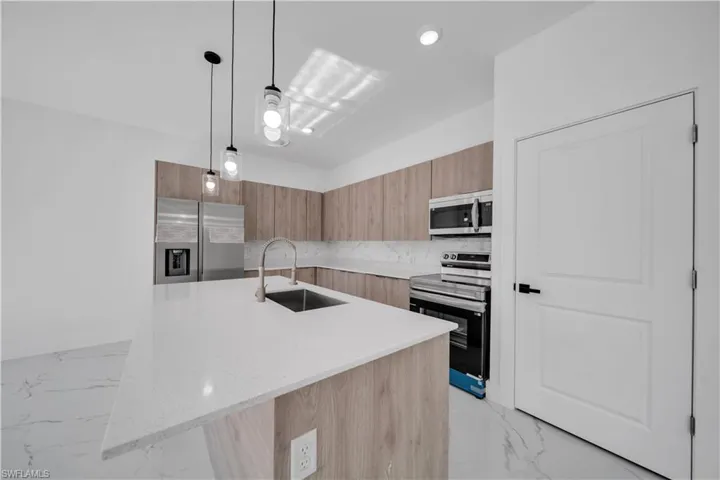 Kitchen with modern cabinets, light stone countertops, stainless steel appliances, a center island with sink, and pendant lighting