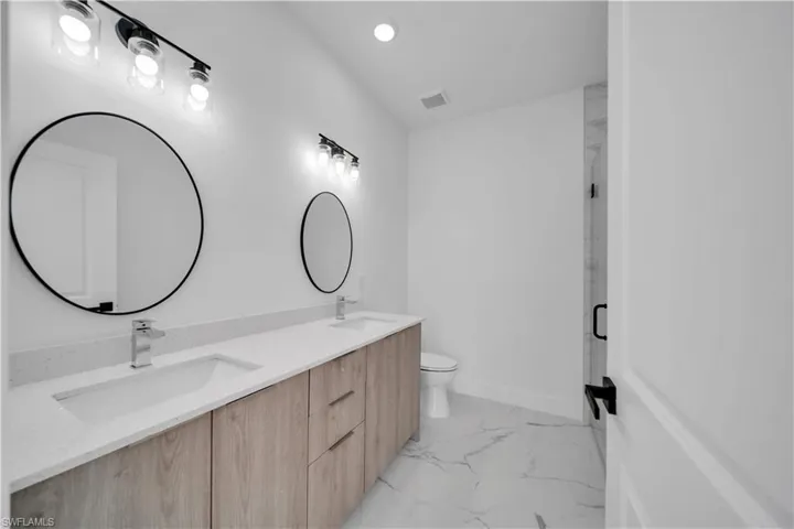 Full bath with double vanity, a marble finish shower, light marble finish floors, and recessed lighting
