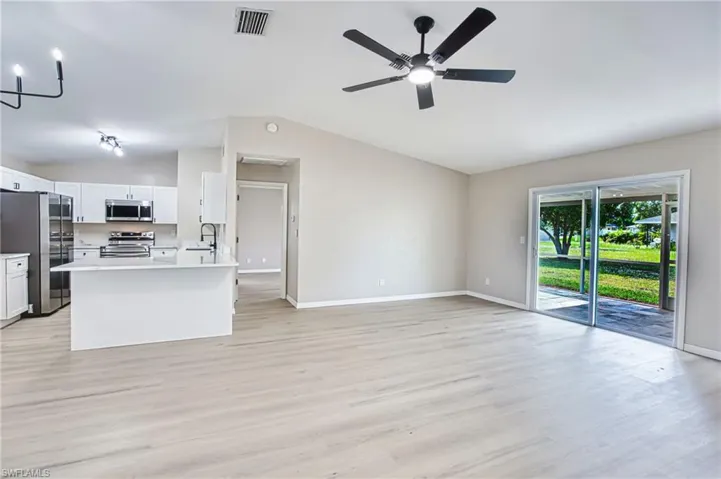 Kitchen with open floor plan, appliances with stainless steel finishes, light wood-type flooring, white cabinets, and a ceiling fan