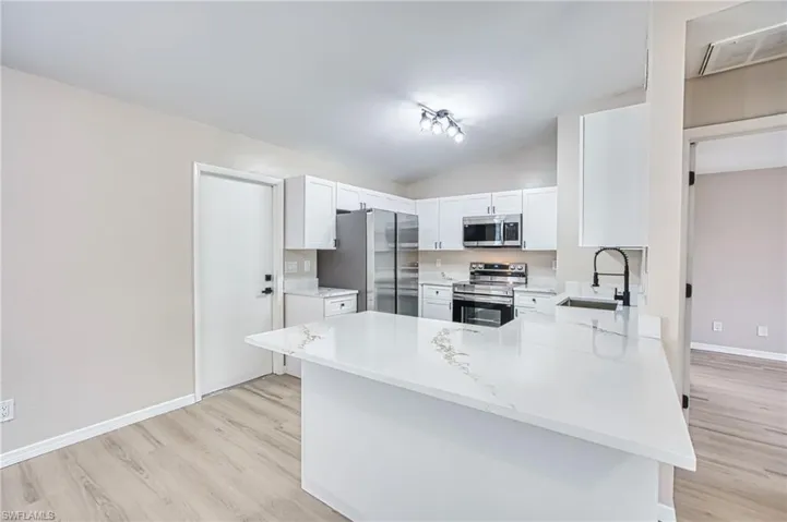 Kitchen featuring appliances with stainless steel finishes, a peninsula, vaulted ceiling, light wood-style floors, and light stone countertops
