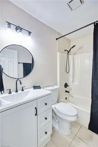 Bathroom featuring light tile patterned flooring, shower / bath combination with curtain, and vanity