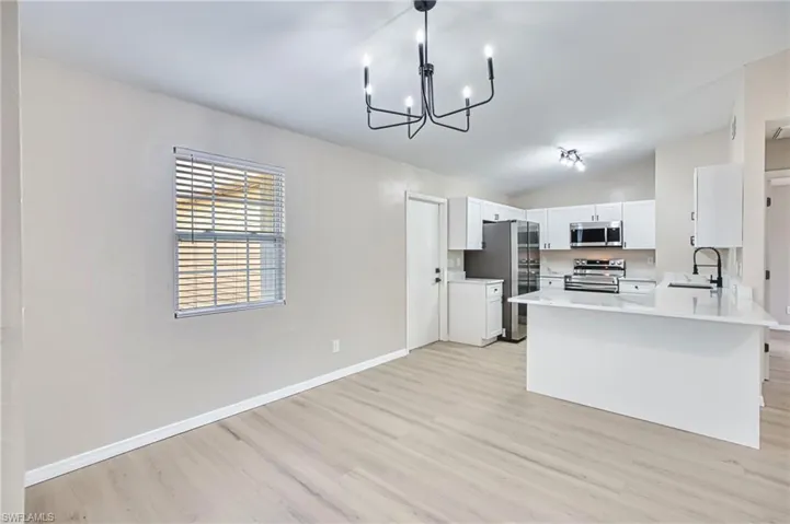 Kitchen with stainless steel appliances, lofted ceiling, a peninsula, light wood-style floors, and white cabinets