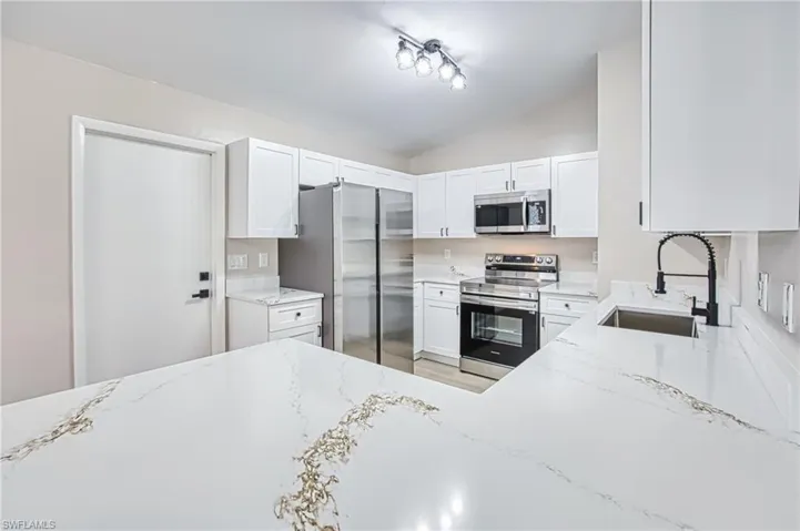 Kitchen featuring appliances with stainless steel finishes, light stone countertops, lofted ceiling, and white cabinets