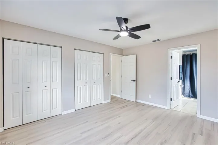 Unfurnished bedroom with multiple closets, light wood-style flooring, ceiling fan, and ensuite bath