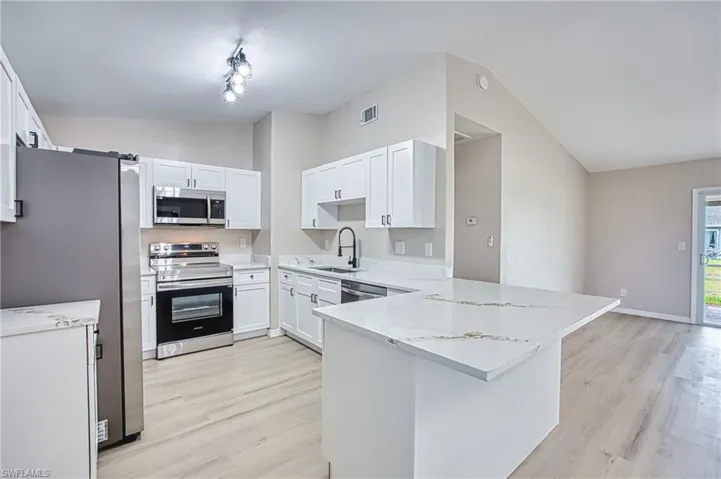 Kitchen with lofted ceiling, appliances with stainless steel finishes, light stone countertops, and light wood-style flooring