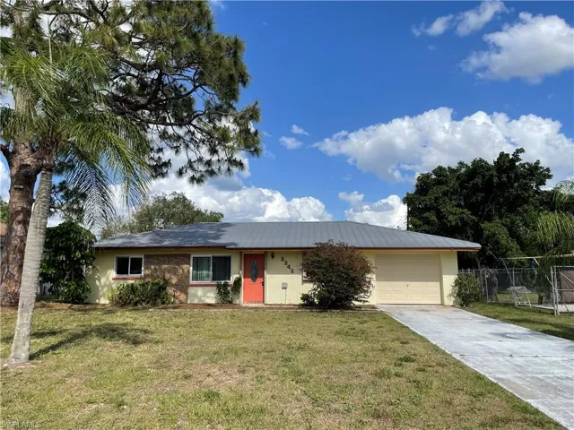 Ranch-style home with concrete driveway, a front yard, a garage, metal roof, and fence