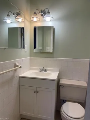 Bathroom featuring toilet, tile walls, vanity, and a wainscoted wall