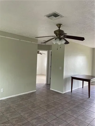 Empty room with visible vents, baseboards, a ceiling fan, and a textured ceiling