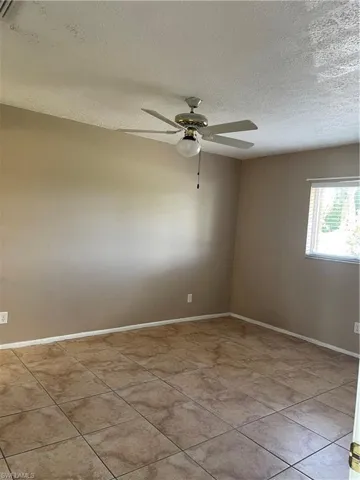 Empty room featuring baseboards, a textured ceiling, light tile patterned flooring, and ceiling fan