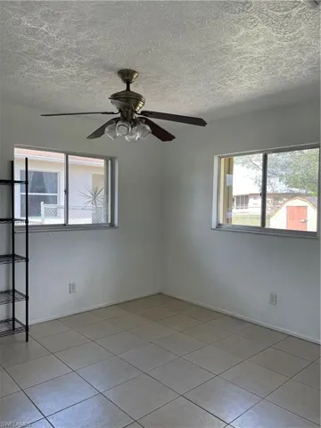 Spare room with a wealth of natural light, tile patterned flooring, a textured ceiling, and ceiling fan