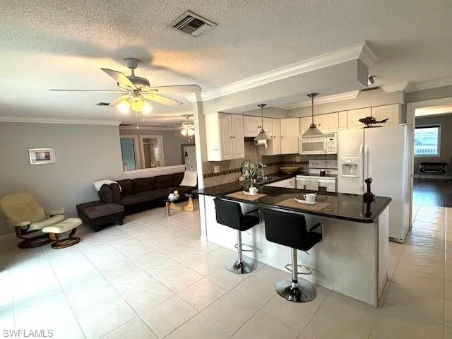 Kitchen with ornamental molding, white appliances, kitchen peninsula, decorative light fixtures, and a breakfast bar