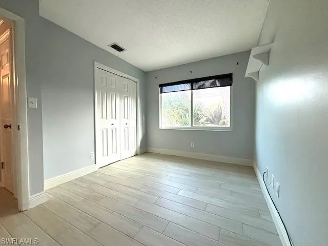 Unfurnished bedroom with light hardwood / wood-style floors, a textured ceiling, and a closet