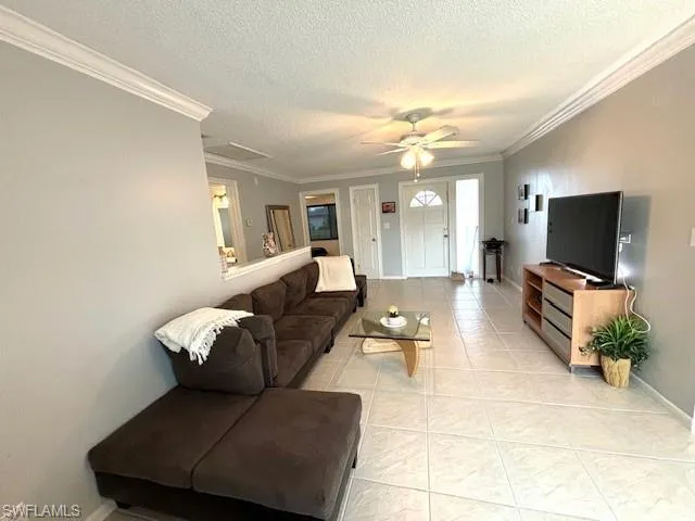 Tiled living room featuring a textured ceiling, ceiling fan, and crown molding