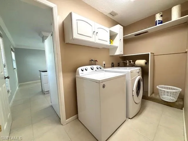 Laundry area with washer and dryer, cabinets, crown molding, hookup for a washing machine, and light tile flooring