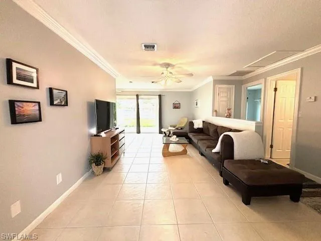 Living room with a textured ceiling, ceiling fan, crown molding, and light tile floors