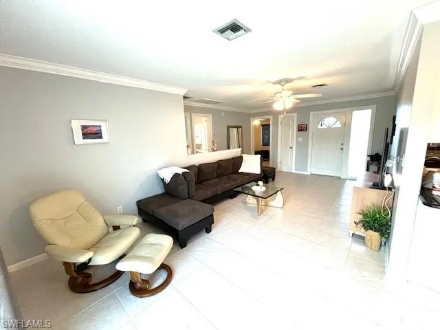 Tiled living room featuring ceiling fan and crown molding