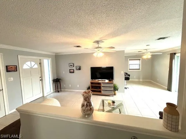 Living room featuring crown molding, tile flooring, ceiling fan, and a textured ceiling