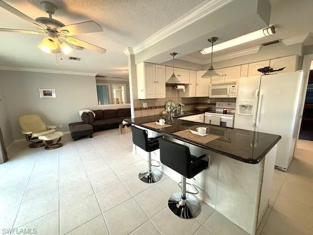 Kitchen with backsplash, a kitchen breakfast bar, hanging light fixtures, ornamental molding, and white appliances