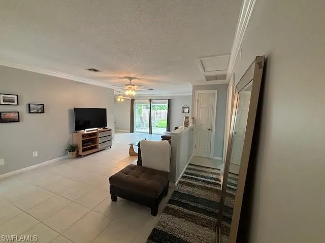 Living room with ceiling fan, ornamental molding, a textured ceiling, and light tile floors