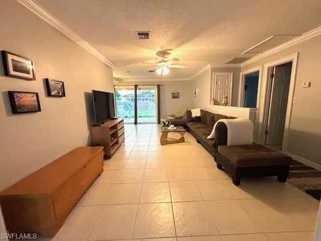 Living room featuring light tile floors, ceiling fan, a textured ceiling, and crown molding