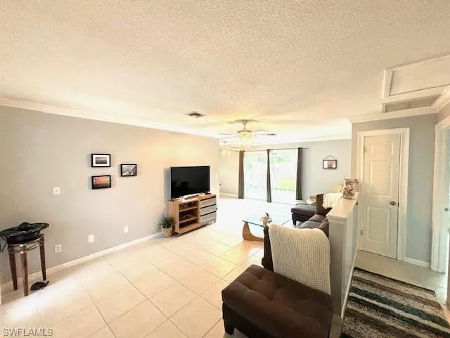 Living room featuring a textured ceiling, ceiling fan, crown molding, and light tile floors