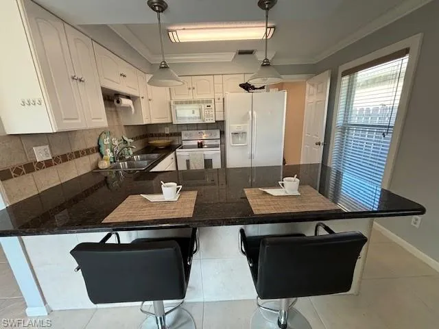 Kitchen with backsplash, white cabinets, white appliances, and kitchen peninsula