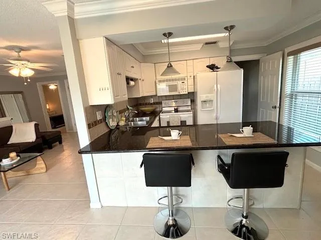 Kitchen with ceiling fan, kitchen peninsula, white appliances, crown molding, and white cabinets