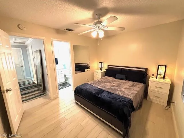 Bedroom featuring ceiling fan, connected bathroom, a textured ceiling, and light wood-type flooring