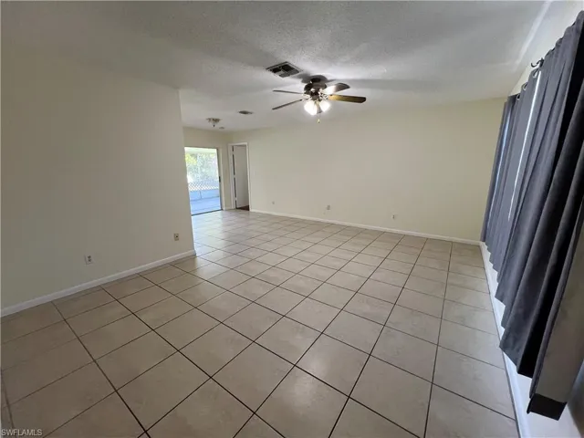 Living room with ceiling fan, light tile patterned flooring, and a textured ceiling
