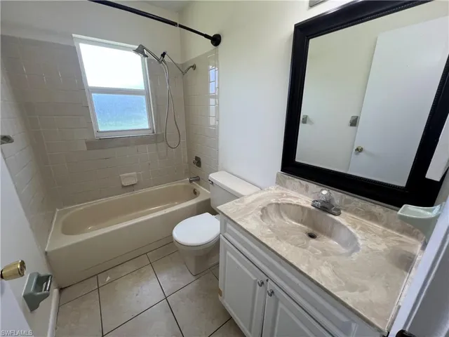 Full bathroom with toilet, tile patterned floors, vanity, and tiled shower / bath